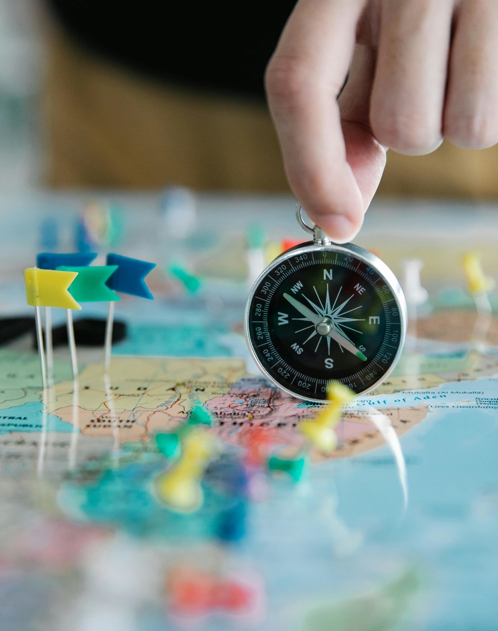 Compass Image of a hand holding a compass on top of a map with pins in it, signifying the importance of the guidance that a professional coach can provide in the coaching process
